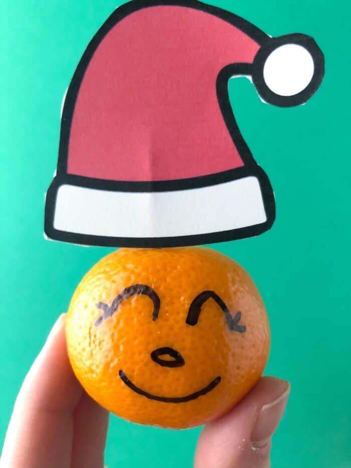 Close up of a clementine with faces drawn on with a Santa hat