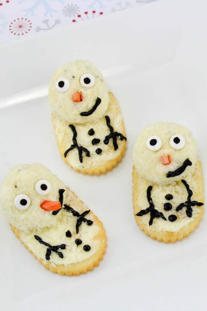Several cheese and crackers decorated like snowmen on a plate.