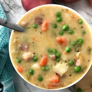 A bowl of potato soup with peas and carrots