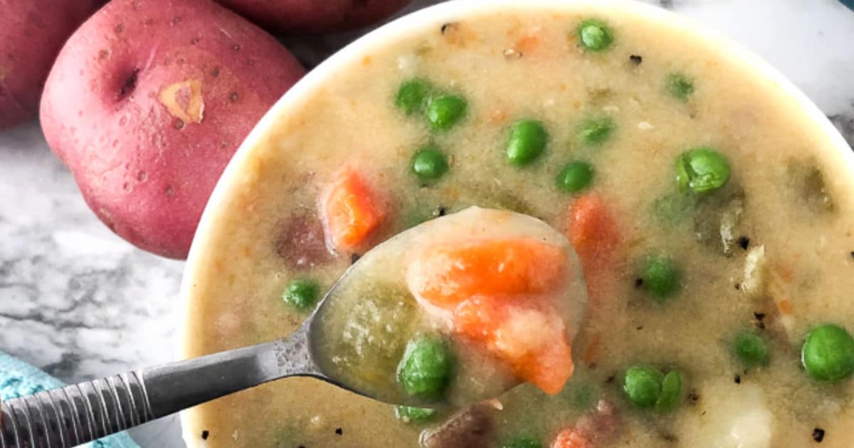 Wide view of a bowl of potato soup with a spoon lifting out a spoonful.