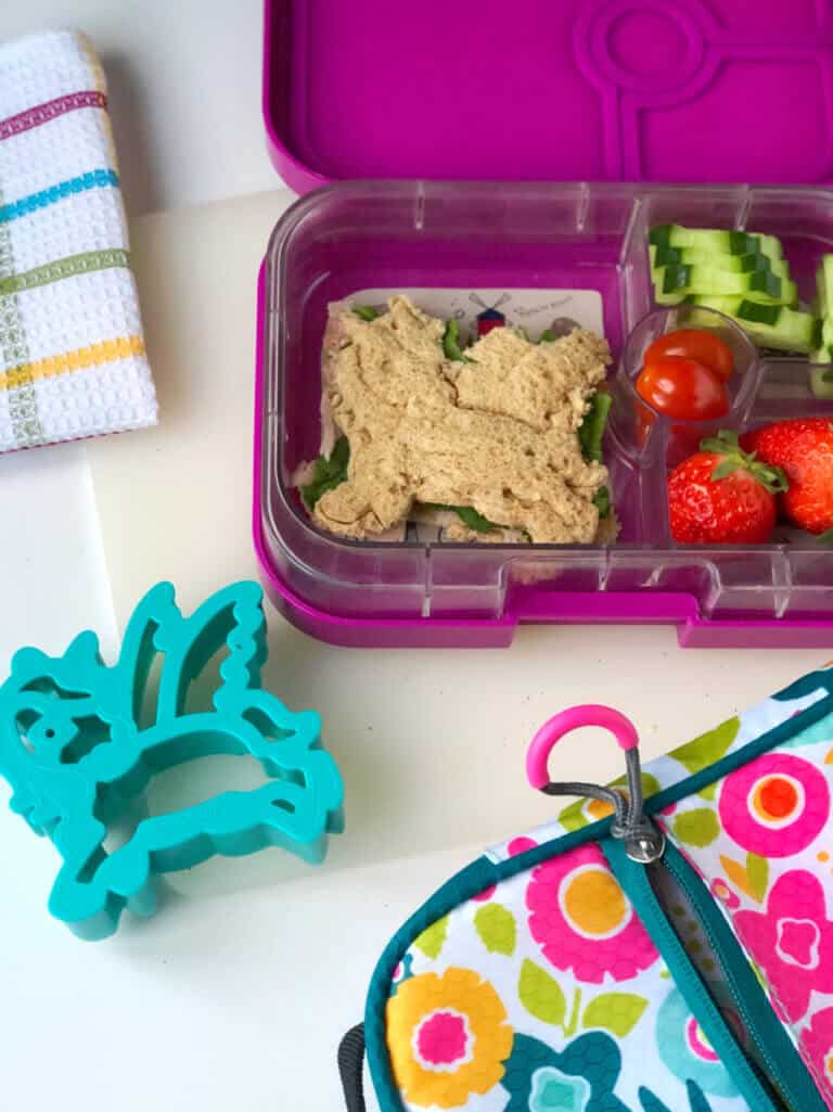 A child's bento lunchbox full of food including a sandwich shaped like a unicorn and a unicorn cookie cutter.