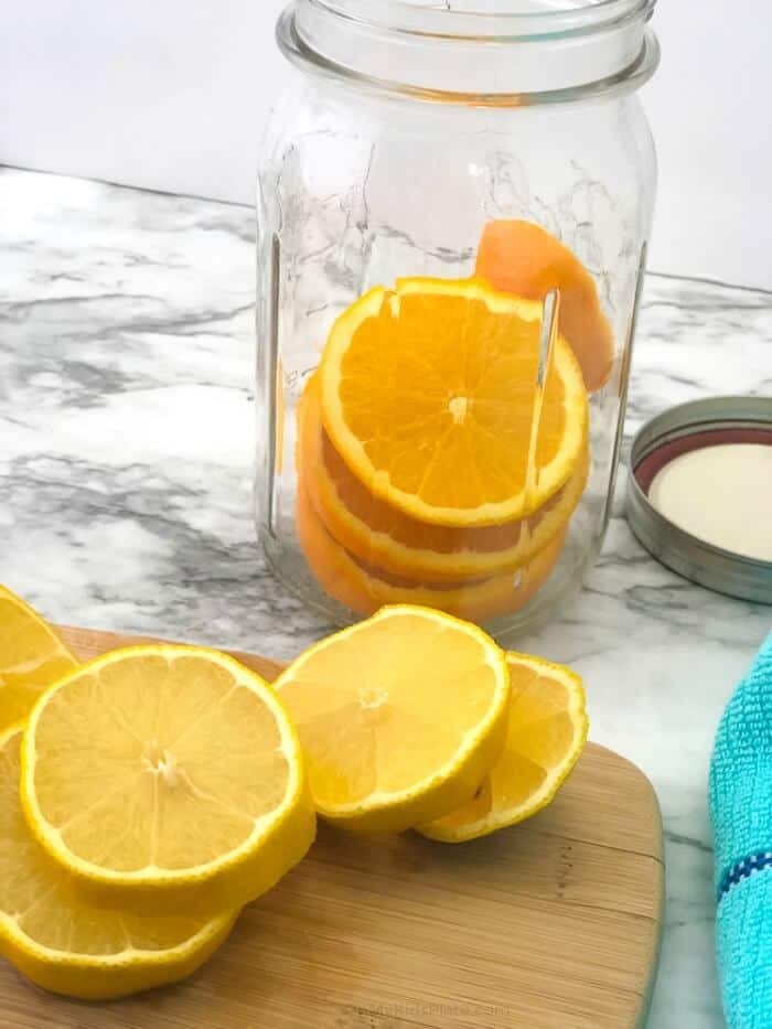 Orange sliced in a large mason jar with more slices on a cutting board