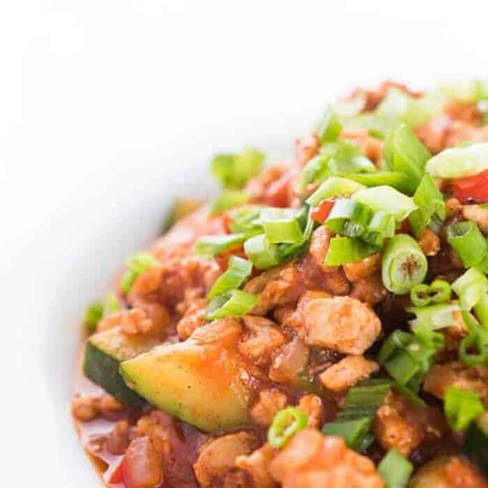 A close up of ground turkey, green onions and zucchini cooked in a red sauce