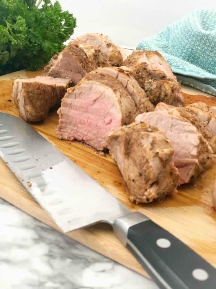 Pork tenderloin on a cutting board cooked and slived next to a knife
