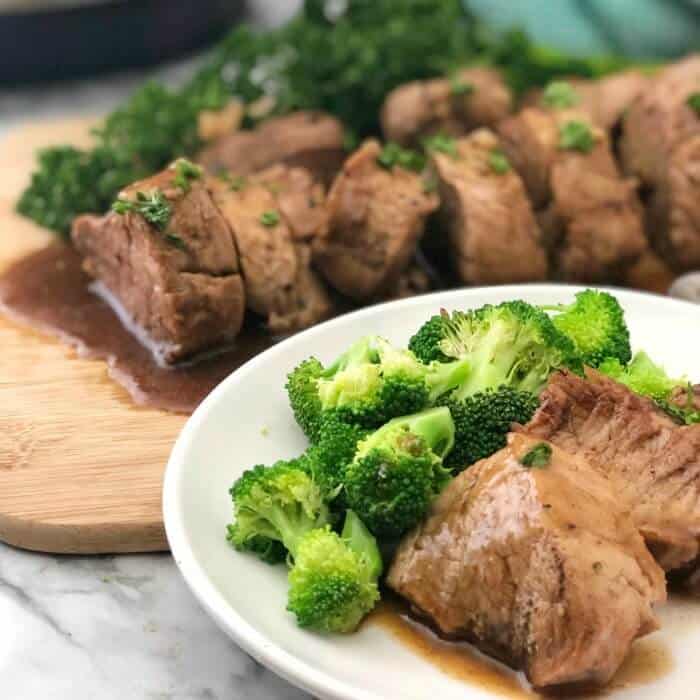 A plate of pork in sauce with broccoli, a cutting board filled with sliced pork behind the plate.