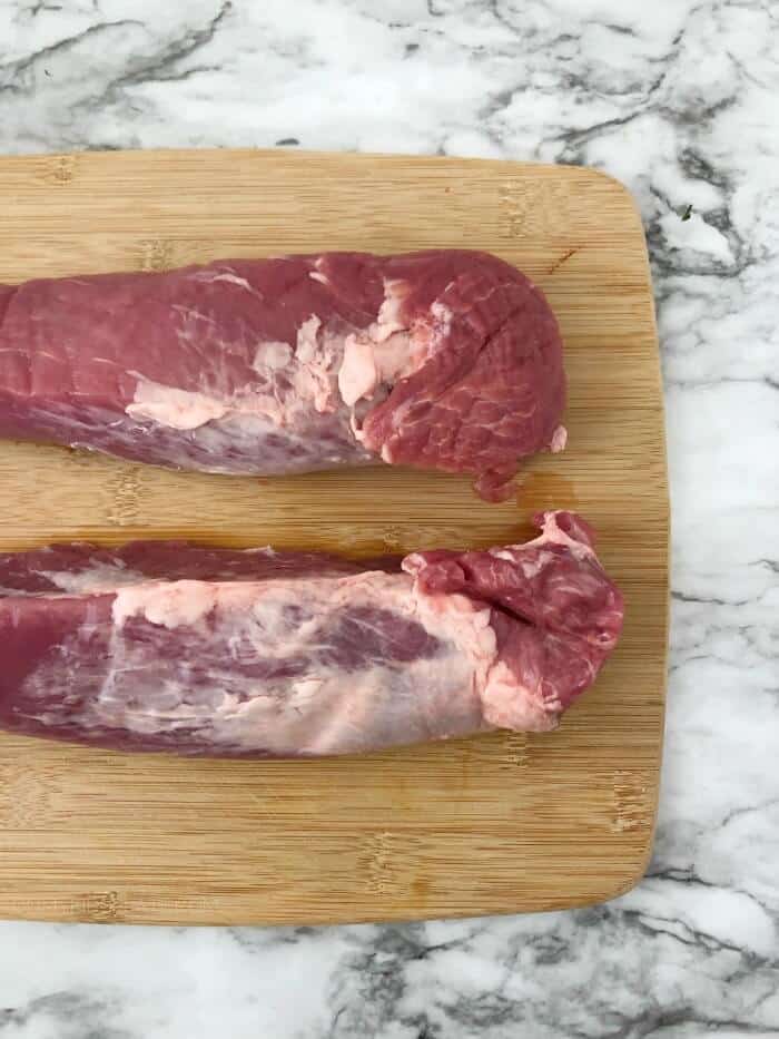 Two pieces of raw pork tenderloin on a cutting board.