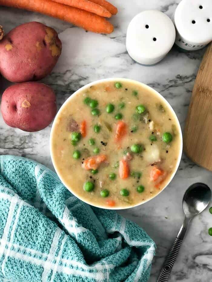 A bowl of soup with potatoes, a spoon and salt and pepper nearby