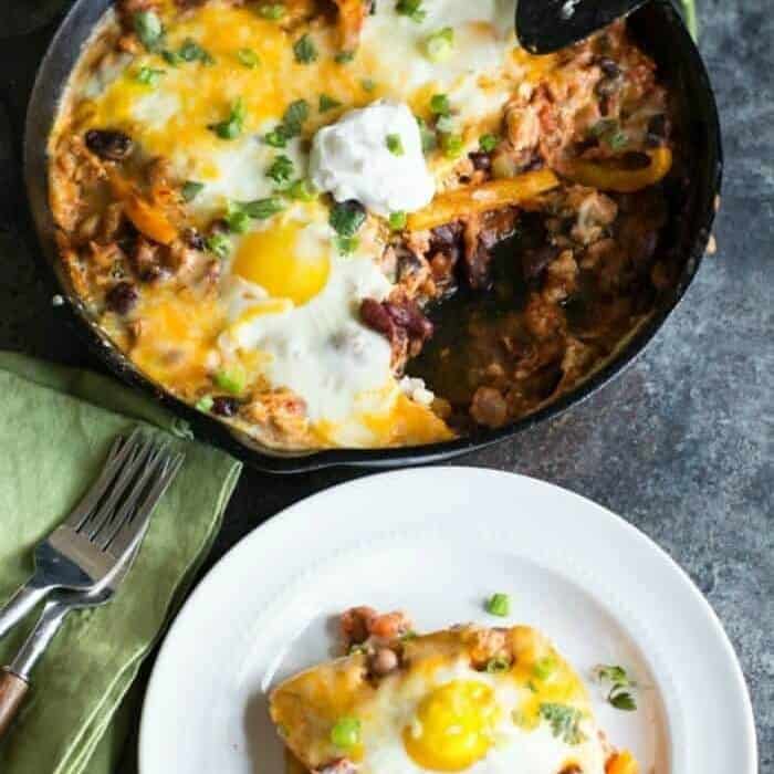 A skillet full of ground turkey topped with sunny side up eggs and cheese next to a plate with a serving.