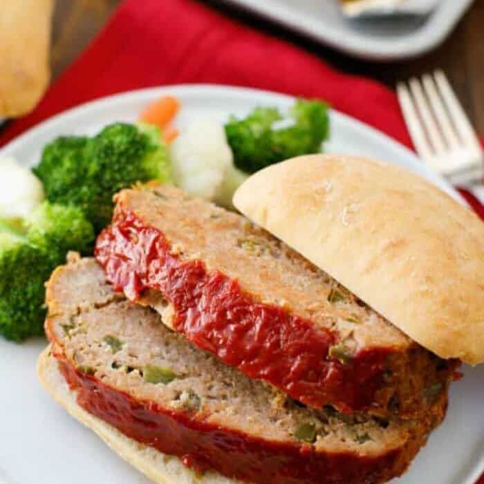 Meatloaf on a bun next to vegetables.