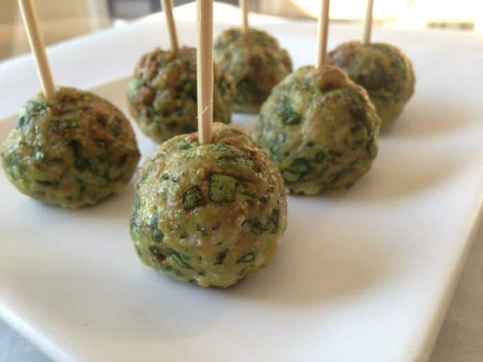 Small meatballs with spinach on toothpicks on a platter.