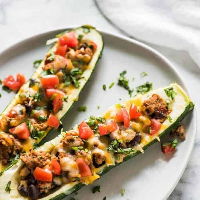 Zucchini slices on a plate hollowed out and filled with turkey, cheese, and tomatoes.