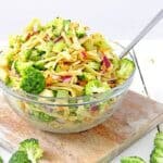 A bowl full of broccoli apple salad with pasta sits on a cutting board coated in a lightly tangy apple cider vinegar and yogurt dressing.