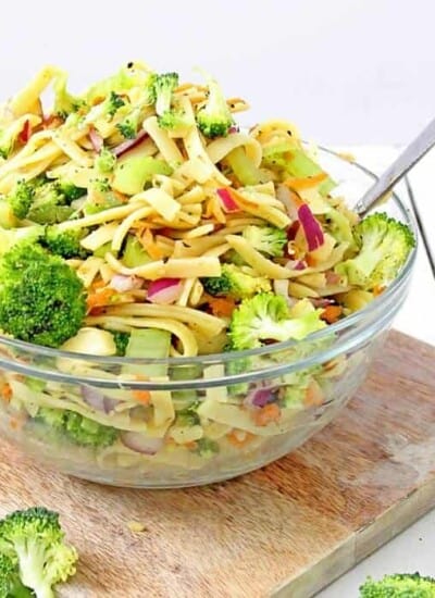 A bowl full of broccoli apple salad with pasta sits on a cutting board coated in a lightly tangy apple cider vinegar and yogurt dressing.