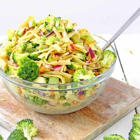 A bowl full of broccoli apple salad with pasta sits on a cutting board coated in a lightly tangy apple cider vinegar and yogurt dressing.