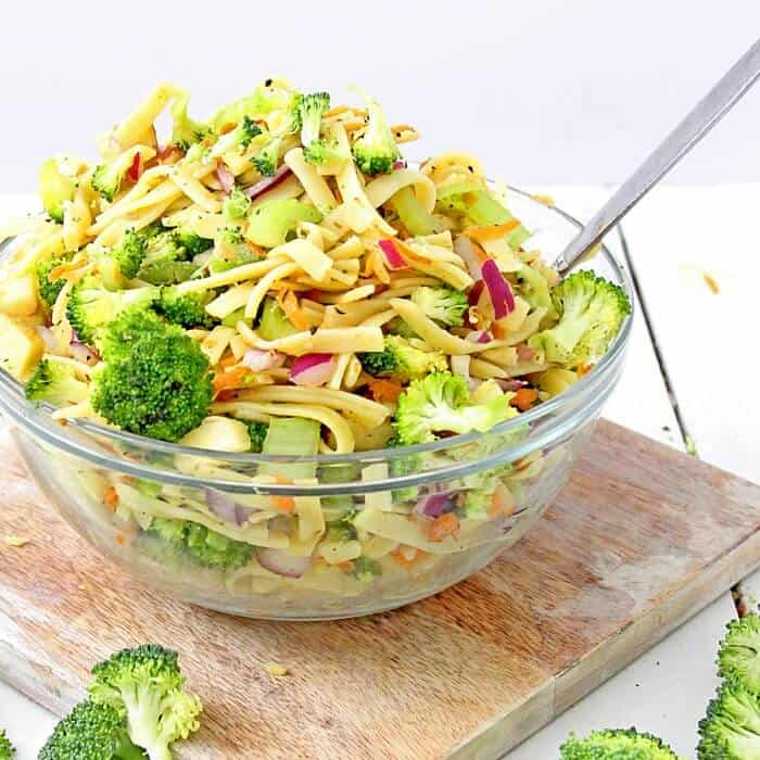 A bowl full of broccoli apple salad with pasta sits on a cutting board coated in a lightly tangy apple cider vinegar and yogurt dressing.