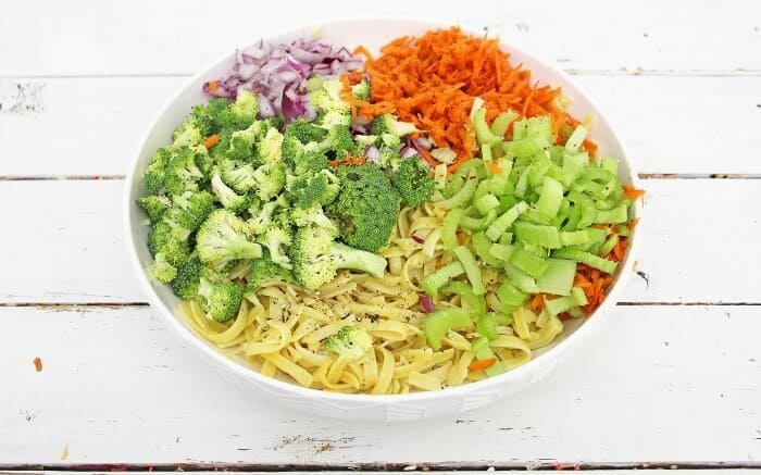 A bowl of chopped vegetables including carrot, cabbage, broccoli, celery and pasta before mixing.