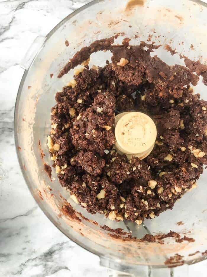 A food processing bowl full of chocolate walnut energy bite dough.