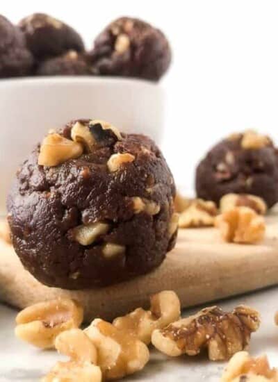 Chocolate walnut energy bite in front of a bowl of energy bites sitting next to walnuts.