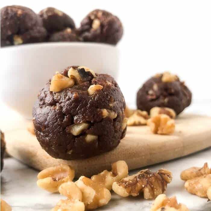 Chocolate walnut energy bite in front of a bowl of energy bites sitting next to walnuts.