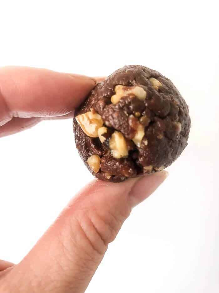 A close up photo as a hand holds up an energy bite made with chocolate, walnuts and peanut butter.
