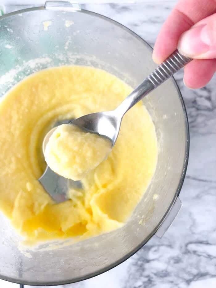 A spoon scooping frozen dole whip out of the top of a food processor from overhead.