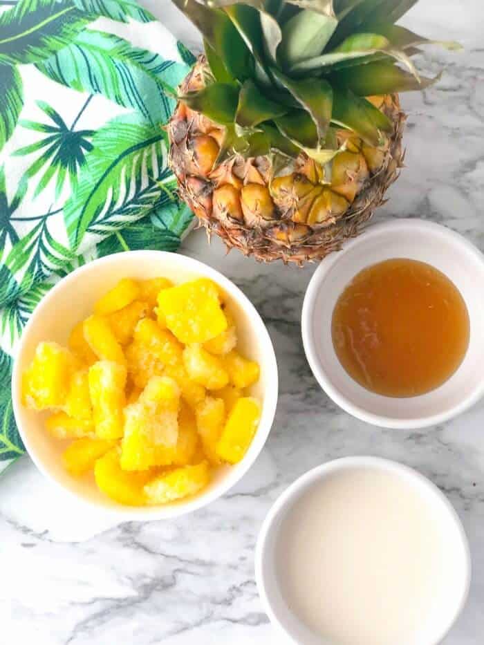 Frozen pineapple sliced, almond milk, honey in bowls and fresh pineapple from overhead.