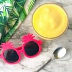 A pineapple dole whip smoothie form overhead next to kids' sunglasses, a towel and a spoon.