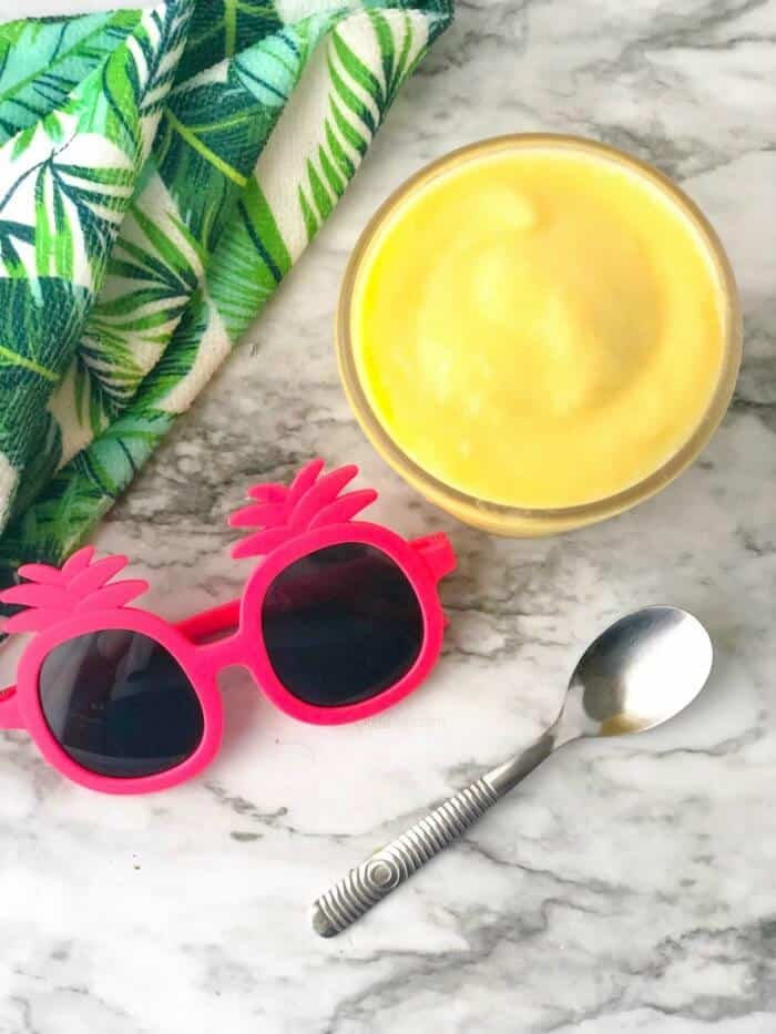 A pineapple smoothie form overhead next to kids glasses, a towel and a spoon.