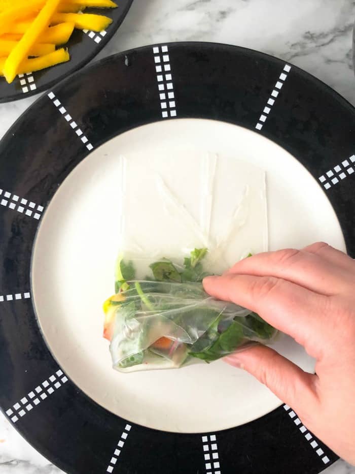 Folding both sides of the spring roll wrapper in and rolling it up on a plate