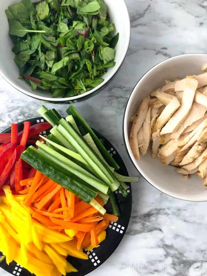 Vegetables on a platter and chicken both sliced thin with a bowl of shredded greens.