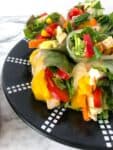 A plate of fresh spring rolls cut in half full of mango, pepper, chicken and spinach