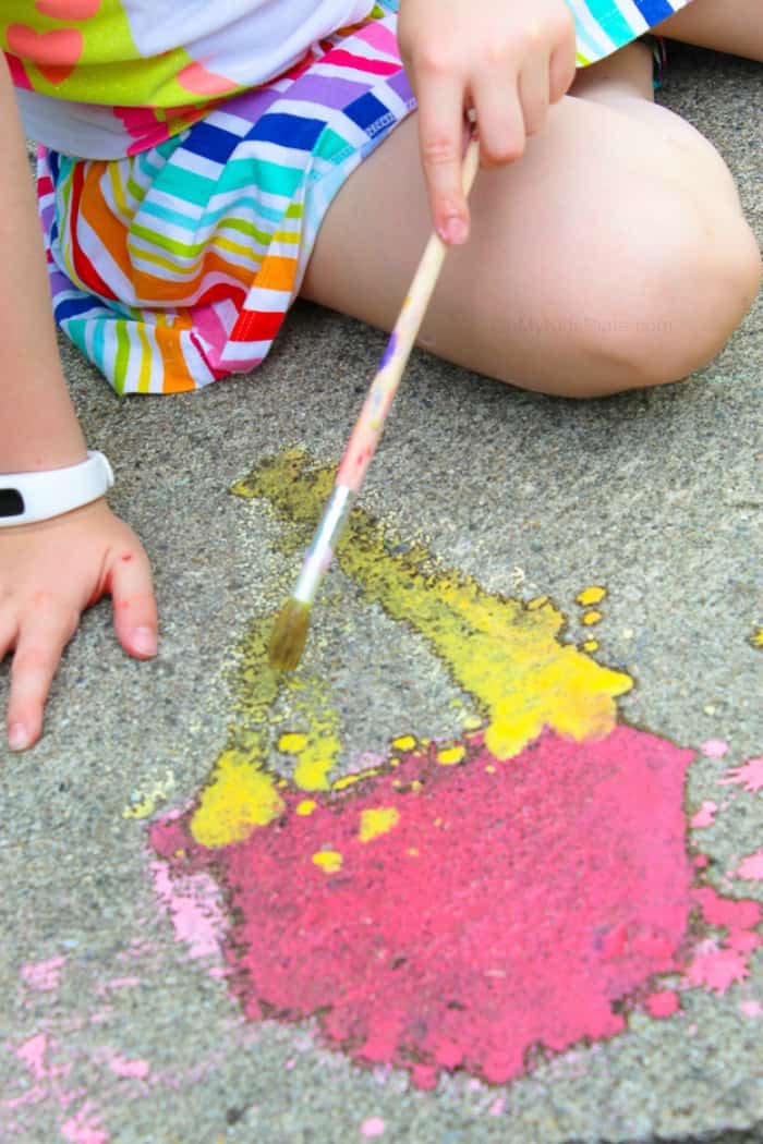Using homemade sidewalk chalk paint, a child paints ice cream cone art on the pavement.