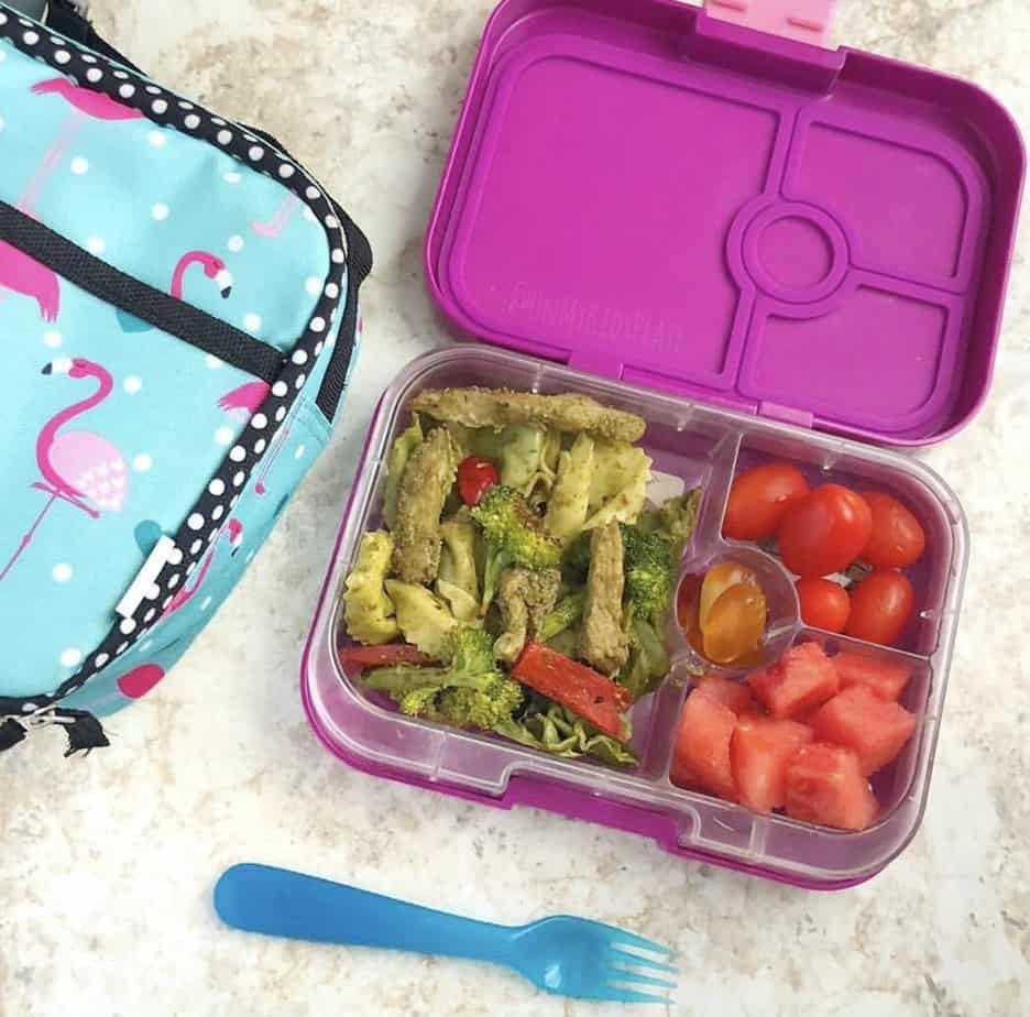 A kid\'s bento lunchbox filled with pesto pasta with chicken, tomatoes and gummies next to an insulated lunchbox and a blue fork