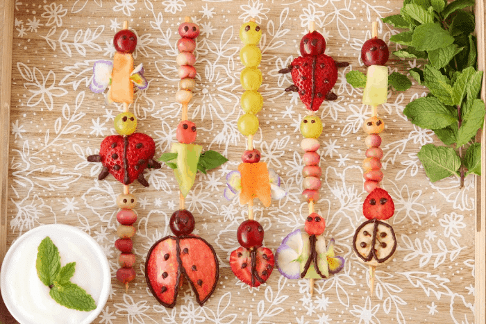 Five fruit skewers decorated like ladybugs, caterpillars and other insects.