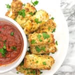 Mozzarella cheese sticks on a plate overhead next to a bowl of sauce topped with parsley