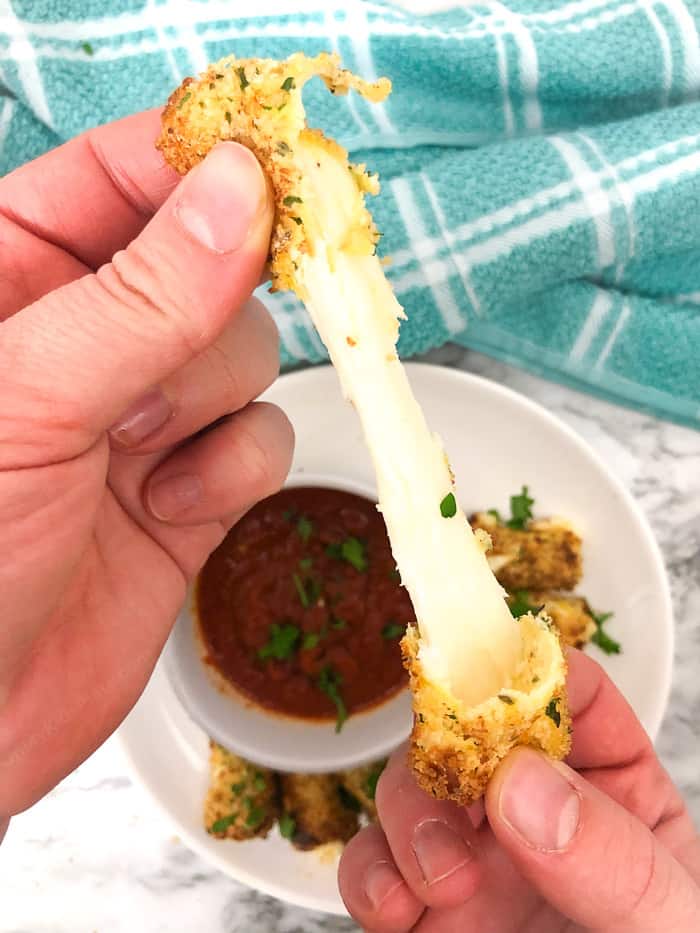 Mozzarella cheese being stretched over a bowl of red sauce and platter of cheesesticks