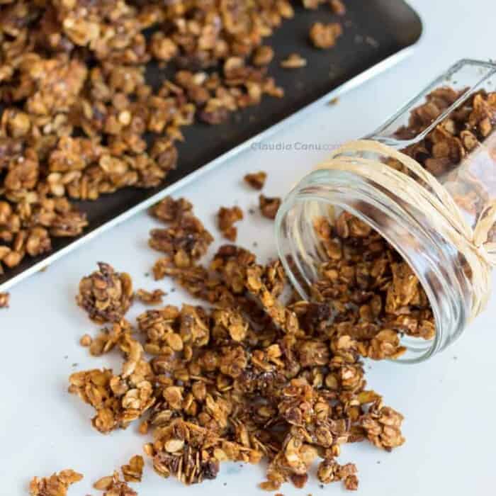 granola spilling out of a glass jar next to a baking sheet full of granola