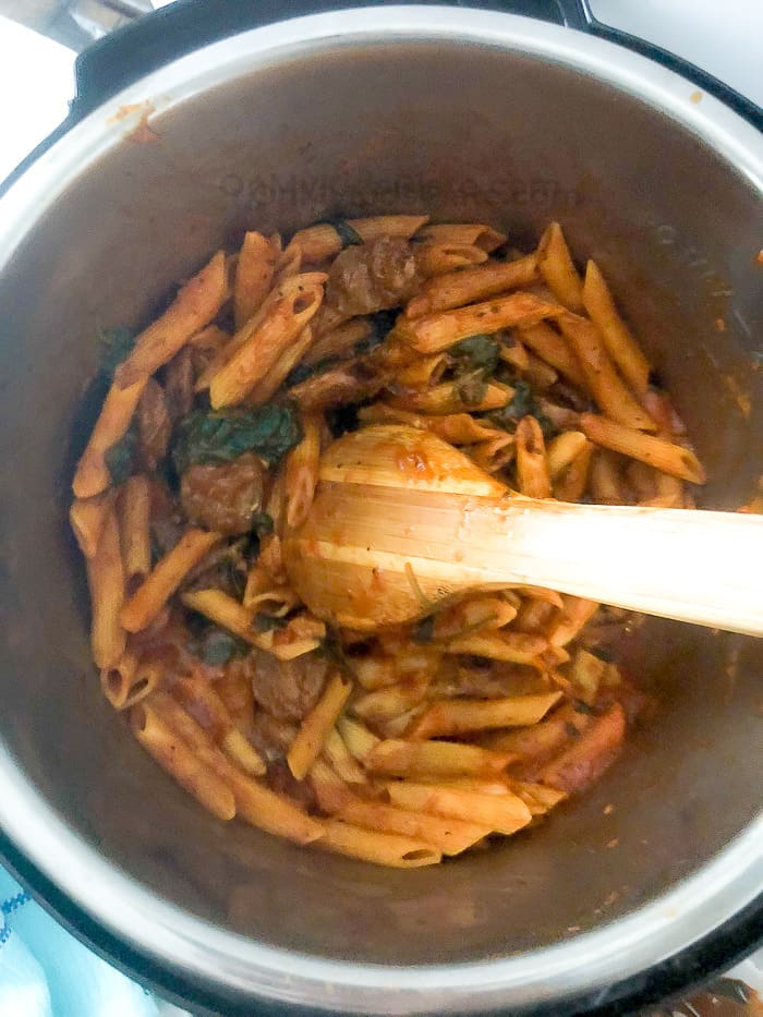 An above view of an instant pot full of pasta being stirred with a wooden spoon