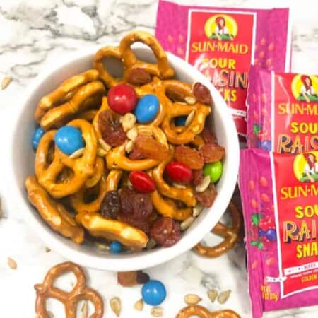 Pretzels, raisings and chocolate pieces in a bowl next to pouches of raisins