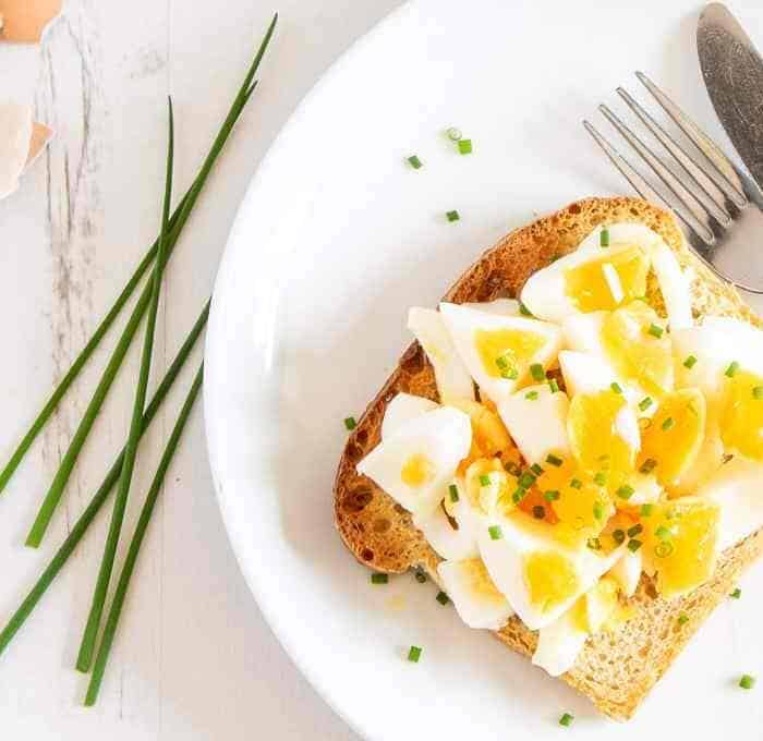 Cooked hardboiled eggs with slightly runny yolks chopped up on toast on a plate