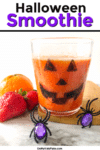 Close up of a jack o lantern glass full of orange smoothie next to fruit and spide rrings