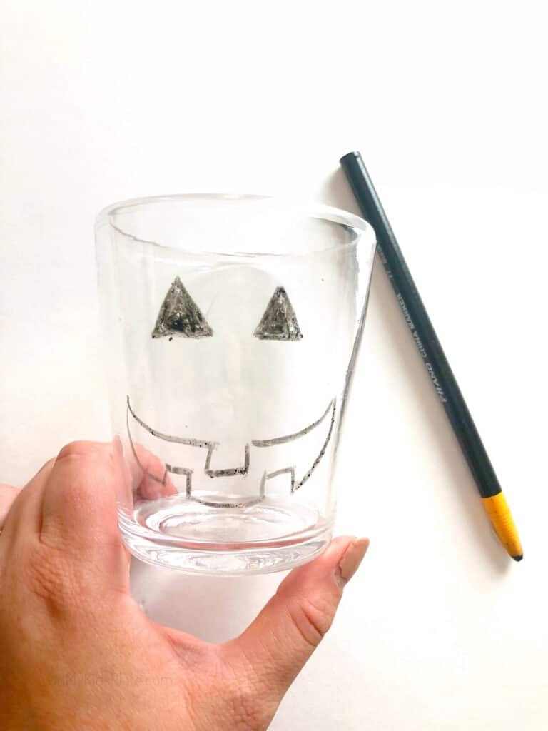 Drawing a jack-o-lantern face on a clear glass with a wax pen.
