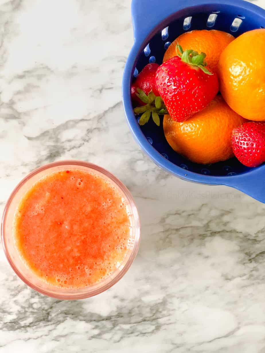 Overhead of a smoothie next to a bowl of oranges and strawberries