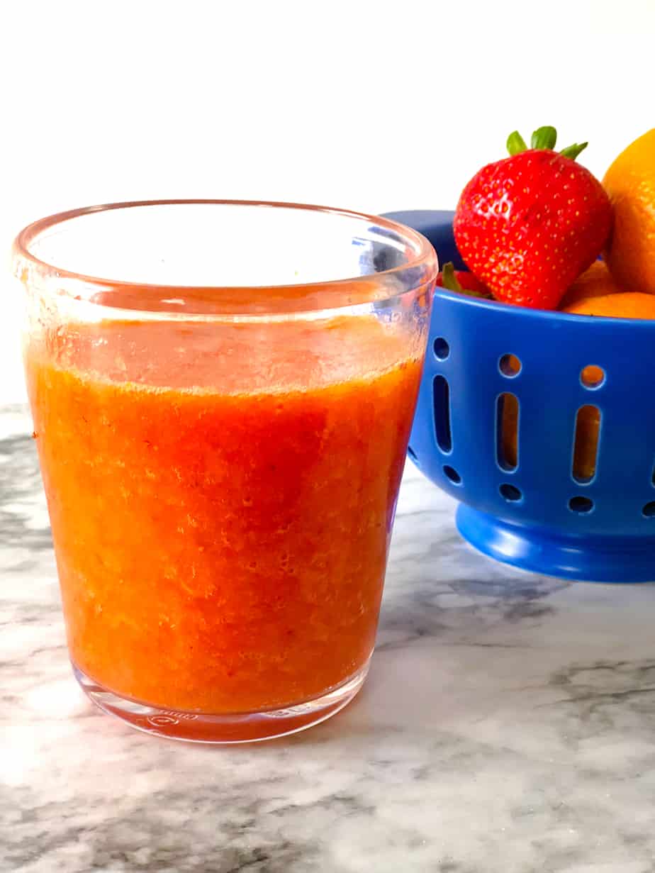 Side view of a clementine strawberry smoothie next to a colander full of more fruit