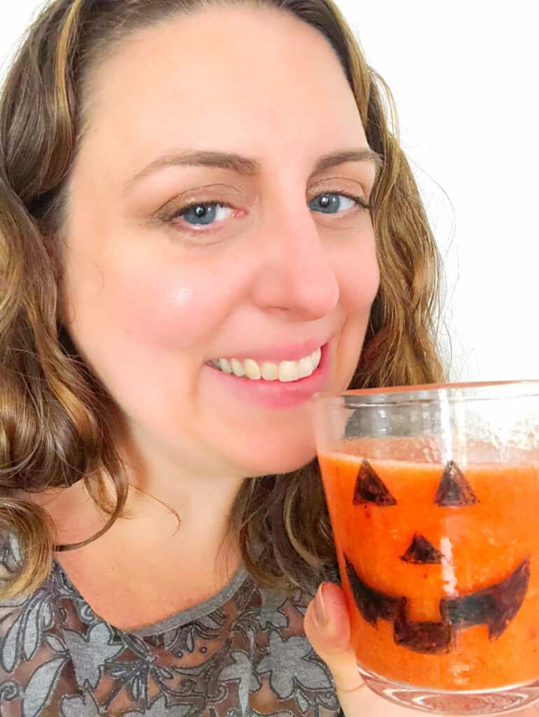 Women drinks orange smoothie with jack o lantern on the glass
