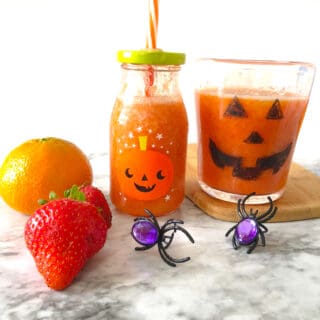 orange smoothie in a cup and milk glass decorated like pumpkins next to fruit and spider rings