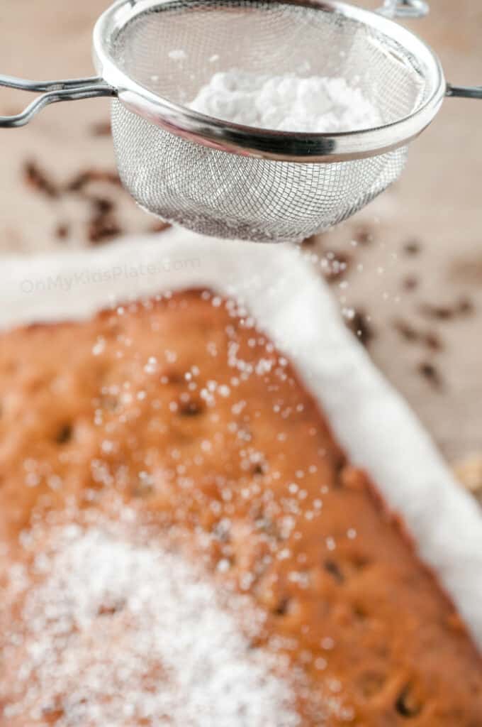 Powdered sugar is sifted through a sieve to add to the top of the apple walnut cake.