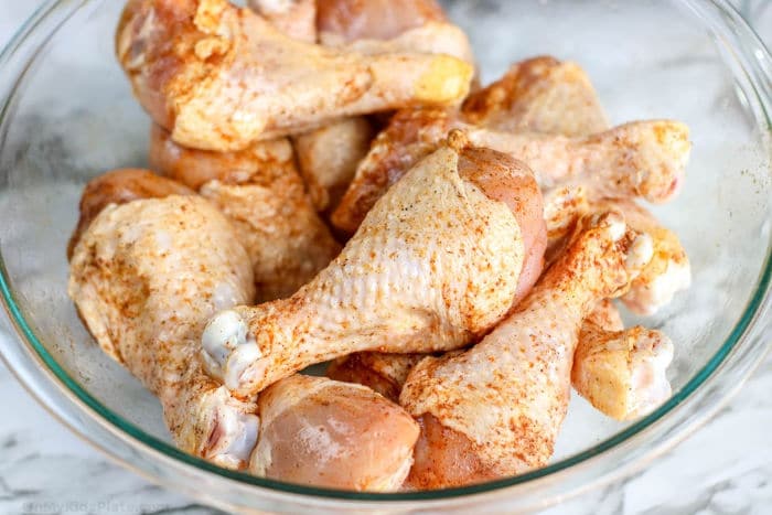 Chicken drumsticks uncooked close up in a bowl with seasoning added