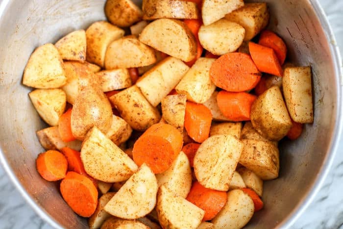 Chopped potatoes and carrots uncooked close up in a bowl with seasoning