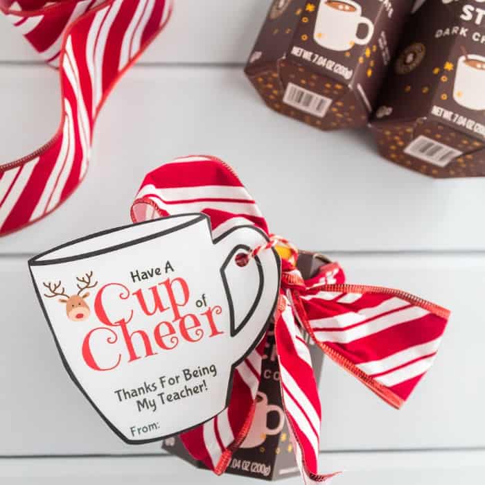 A hot chocolate gift dressed up with a ribbon bow and a Christmas mug shaped gift tag